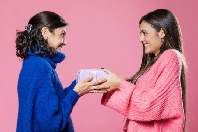mom and daughter exchanging a gift against a pink background